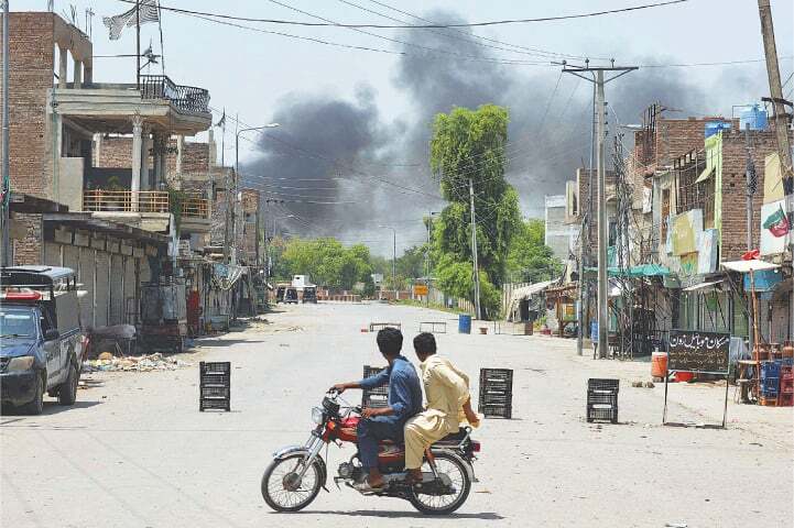 Men riding a bike turn back from a roadblock as they watch smoke rising, following an explosion after suspected militants attempted to storm the Bannu cantonment, on Monday.—AFP